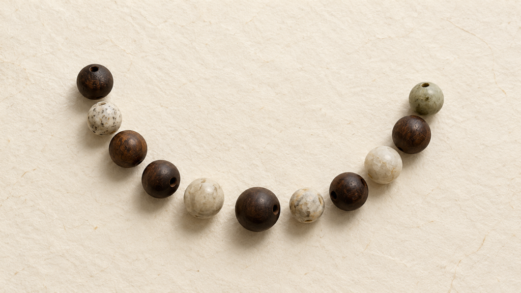 Loose dark and pale beads arranged in an open arc on cream paper, conceptual editorial image.